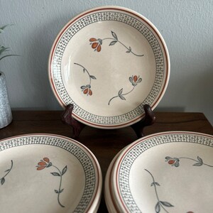 May include: Set of four white ceramic dessert plates with a brown and gray patterned border and a floral design in orange and gray.