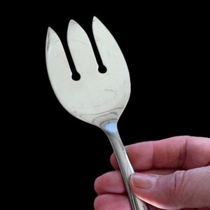 May include: A silver serving fork with three prongs. The fork is designed for serving salad or other foods.