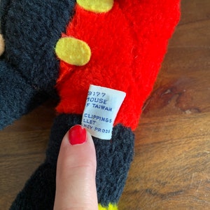 Może przedstawiać: Pluszowa zabawka Mickey Mouse w kolorze czarnym i czerwonym z ż&oacute;łtymi guzikami. Etykieta na zabawce zawiera napis "9177 House Taiwan Clipping's Llet Sney Prods."