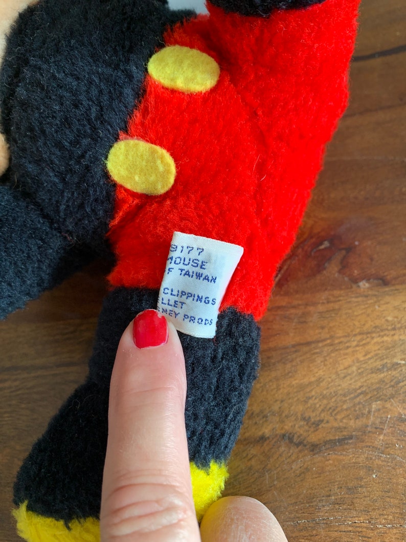 Może przedstawiać: Pluszowa zabawka Mickey Mouse w kolorze czarnym i czerwonym z ż&oacute;łtymi guzikami. Etykieta na zabawce zawiera napis "9177 House Taiwan Clipping's Llet Sney Prods."