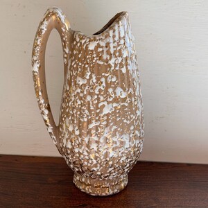 May include: A brown ceramic pitcher with a white and gold speckled glaze. The pitcher has a wide mouth and a handle.