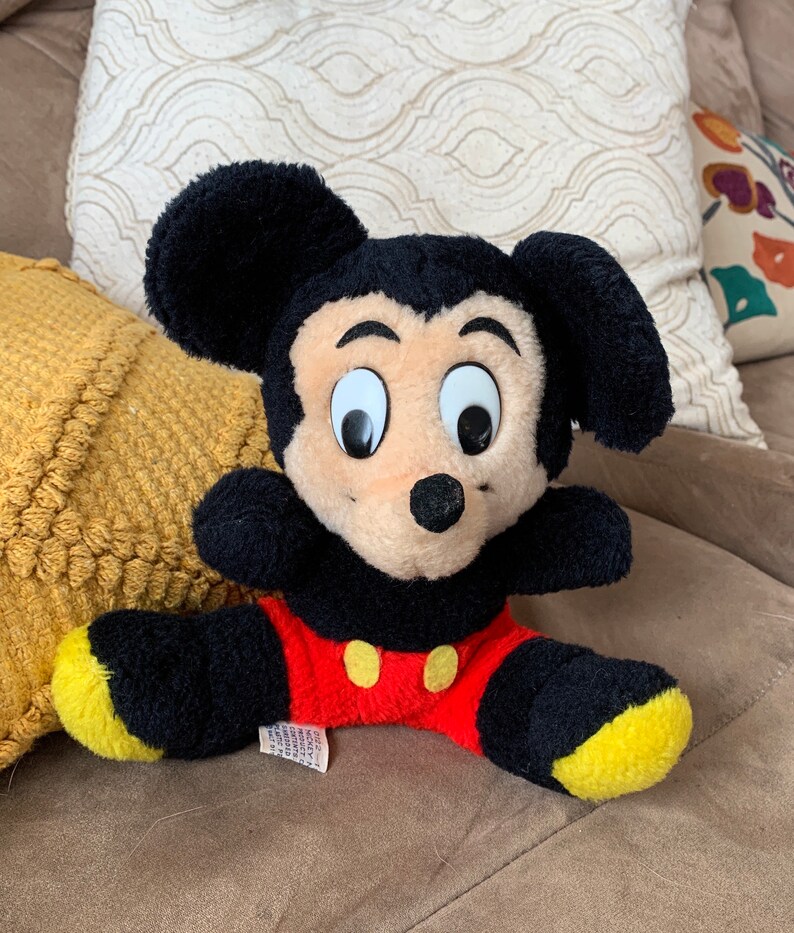 Może przedstawiać: Pluszowa zabawka Mickey Mouse w kolorze czarnym i czerwonym z ż&oacute;łtymi akcentami na uszach i stopach. Zabawka ma czarny nos i duże białe oczy.