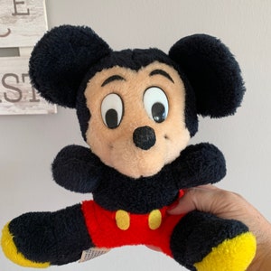Może przedstawiać: Pluszowa zabawka vintage Mickey Mouse z czarnym futerkiem, dużymi białymi oczami i czerwono-ż&oacute;łtym strojem.