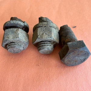 May include: Three weathered metal bolts and nuts. The bolts have hexagonal heads and threaded shafts. The nuts are also hexagonal. The metal has a rusty, aged appearance, suggesting outdoor use or exposure to the elements. The background is a solid orange color.