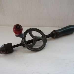 May include: A vintage hand drill with a green wooden handle and a metal crank. The drill bit is attached to a metal chuck.