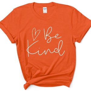 May include: Orange short-sleeved t-shirt with a white graphic that says "Be Kind" with a heart symbol.