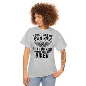 May include: Gray t-shirt with black text that reads "I don't ride my own bike but I do ride my own biker". The text is surrounded by a graphic of a motorcycle with wings.