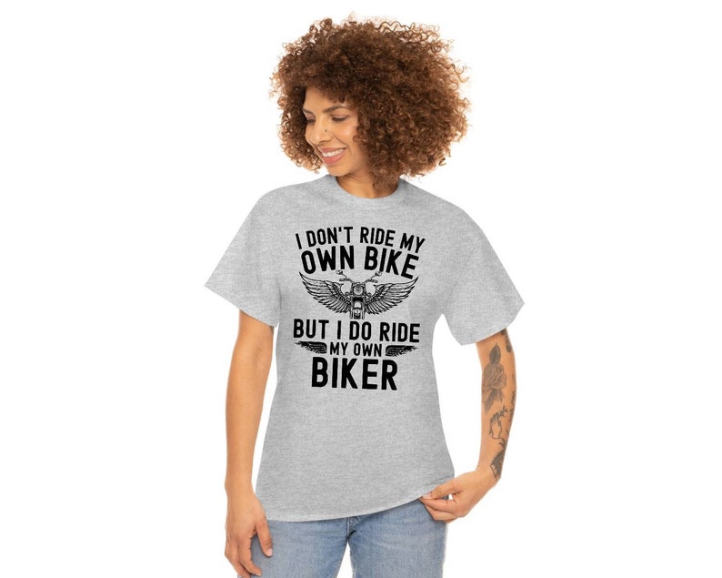 May include: Gray t-shirt with black text that reads "I don't ride my own bike but I do ride my own biker". The text is surrounded by a graphic of a motorcycle with wings.