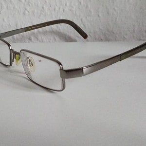Puede incluir: Un par de gafas de color plateado con monturas rectangulares y lentes transparentes.