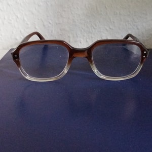 Könnte beinhalten: Braune Kunststoff-Brille mit klaren Gläsern auf einer dunkelblauen Oberfläche.