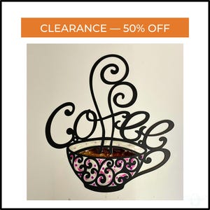 May include: Black metal coffee sign with the word "Coffee" in a cursive font. The coffee cup has a pink and white floral design. The sign has an orange banner at the top that says "CLEARANCE - 50% OFF".