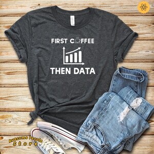 May include: A dark gray t-shirt with the text "FIRST COFFEE THEN DATA" in white. The text is accompanied by a graphic of a coffee cup with steam rising from it and a line graph going up.