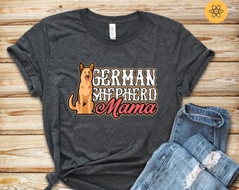 May include: A dark grey t-shirt with the text "GERMAN SHEPHERD Mama" in white and pink lettering. A brown and black German Shepherd dog is sitting to the left of the text.