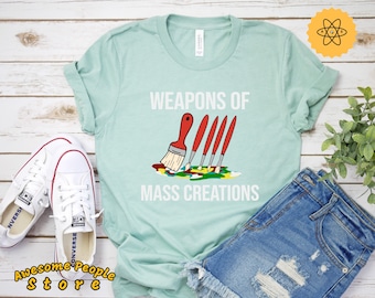 May include: A light blue t-shirt with the text "Weapons of Mass Creations" and a cartoon image of paintbrushes and a paint splattered canvas.