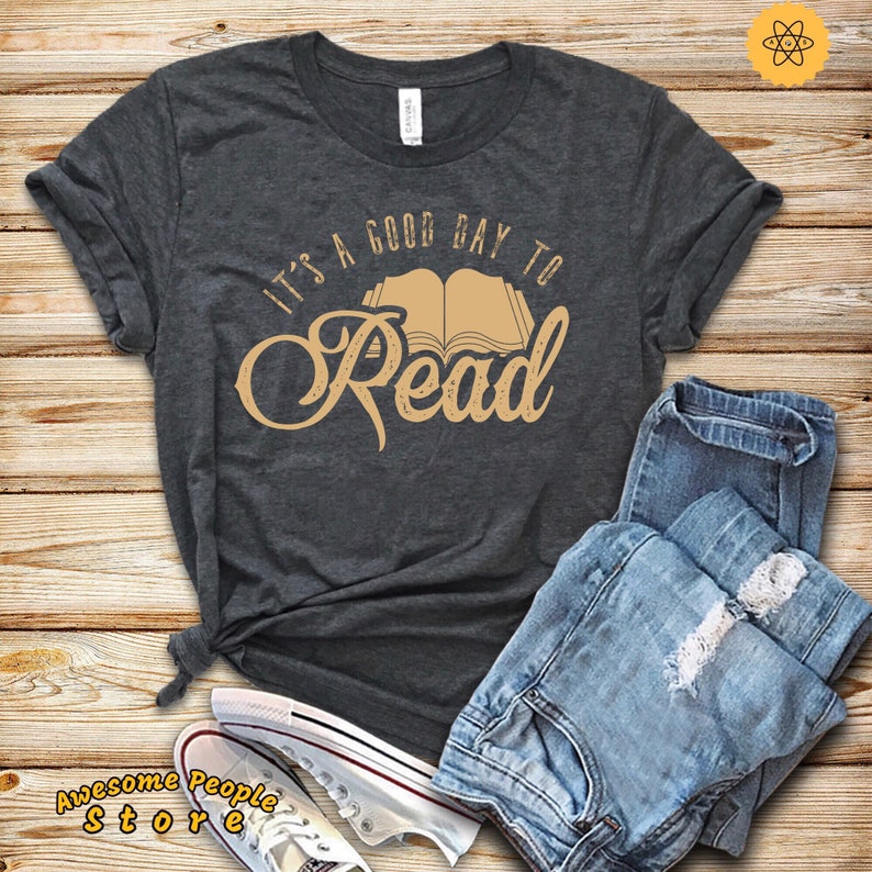 May include: A dark gray t-shirt with the text "It's a good day to read" in a tan color. The text is in a stylized font and includes an illustration of an open book.
