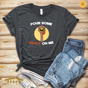 May include: A dark gray t-shirt with the text "POUR SOME GRAVY ON ME" and a cartoon turkey with a red wattle and yellow eyes.