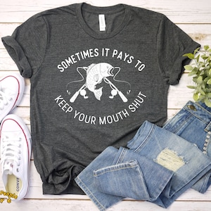 May include: A dark gray t-shirt with a white graphic of a fish on a fishing rod with the text "Sometimes it pays to keep your mouth shut".