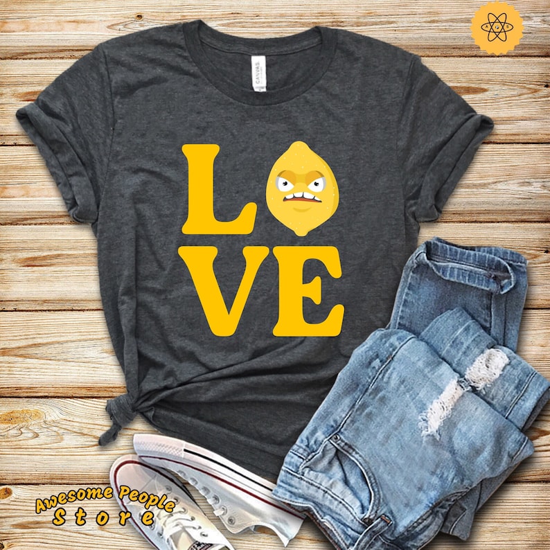 Puede incluir: Una camiseta gris oscuro con la palabra "LOVE" impresa en letras amarillas. La "O" est&aacute; reemplazada por un lim&oacute;n amarillo de dibujos animados con una cara de enfado.