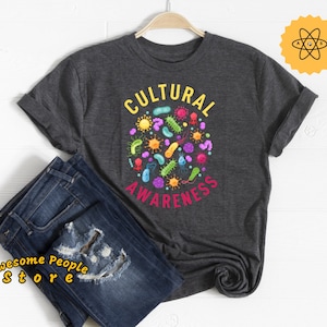 May include: A dark gray t-shirt with the text "CULTURAL AWARENESS" in a circle with colorful bacteria and microbes inside.