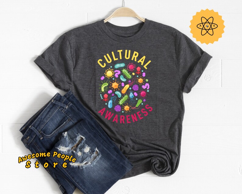 May include: A dark gray t-shirt with the text "CULTURAL AWARENESS" in a circle with colorful bacteria and microbes inside.