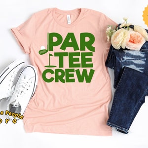 May include: A pink t-shirt with the text "Par Tee Crew" in green letters. The text includes a golf club and ball graphic.