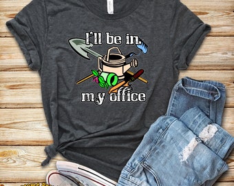 Può includere: Una maglietta grigio scuro con il testo "I'll be in my office" e una grafica di attrezzi da giardinaggio, tra cui una pala, un annaffiatoio e un rastrello.