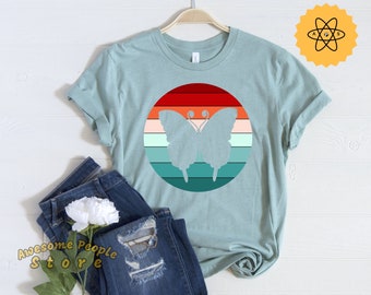 Op de afbeelding: Een lichtblauw t-shirt met een retro-grafische afbeelding van een vlinder in een cirkel met rode, oranje, gele, groene en blauwe strepen.