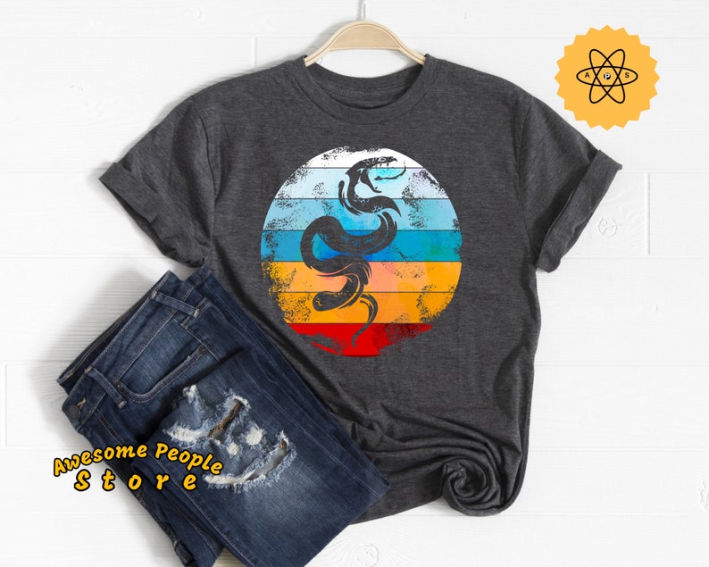 May include: A dark gray t-shirt with a retro-style graphic of a snake on a colorful background. The snake is black and the background is a rainbow of colors, including red, orange, yellow, green, blue, and purple.