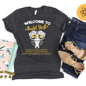Peut inclure: Un t-shirt gris foncé avec un hibou de dessin animé et le texte "Bienvenue au quart de nuit. Où tous les jours sont lundi. Aujourd'hui est hier et demain est aujourd'hui."