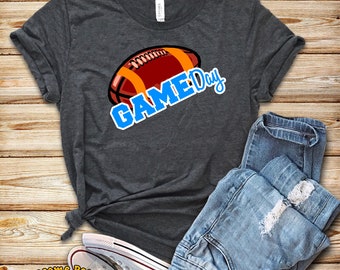 Könnte beinhalten: Ein dunkelgraues T-Shirt mit einem braunen Football und dem Text "GAME Day" in blauen Buchstaben.