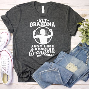 May include: Gray t-shirt with white text that reads "Fit Grandma Just Like A Regular Grandma But Cooler". The shirt features a graphic of a woman lifting weights.