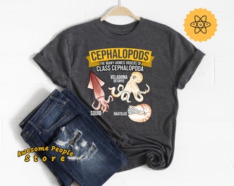 May include: A dark gray t-shirt with a graphic of different cephalopods, including a squid, octopus, and nautilus. The text "Cephalopods" is in a yellow banner at the top of the graphic. The text "The many-armed orders of Class Cephalopoda" is below the banner. The text "Veladona Octopus" is above the octopus graphic. The text "Squid" is below the squid graphic. The text "Nautilus" is below the nautilus graphic.
