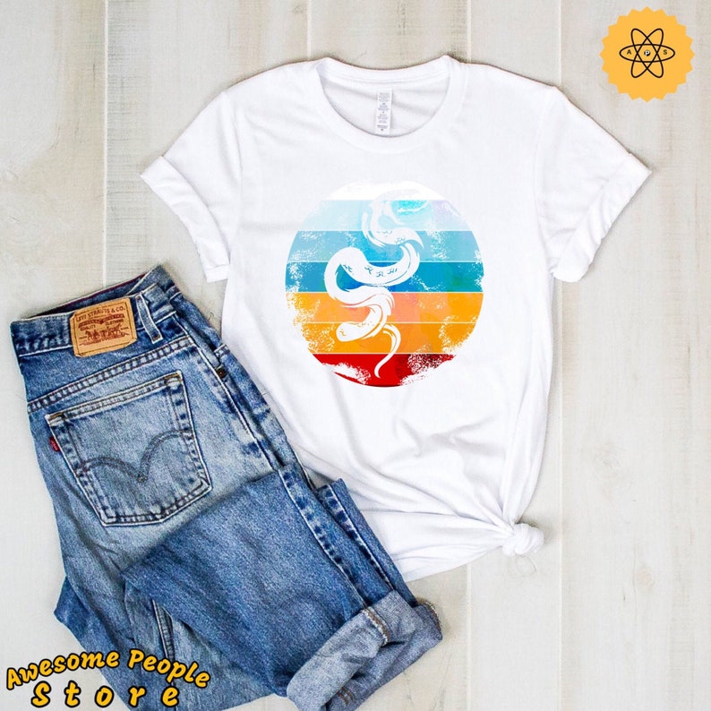 May include: White t-shirt featuring a retro-style graphic of a snake with a colourful sunset background.