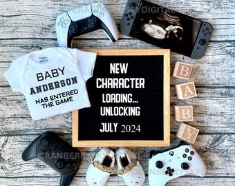 Pode incluir: Um macacão branco com o texto "Baby Anderson Has Entered The Game" nele. Um quadro de letras preto com o texto "Novo Personagem Carregando... Desbloqueio Julho 2024". Um controlador de videogame branco e preto, um Nintendo Switch branco e preto e um conjunto de blocos de madeira que soletram "Baby".