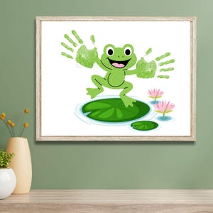 May include: A framed print featuring a cartoon frog jumping on a lily pad. The frog is green with a smiling face and outstretched arms, with green handprints. Pink water lilies and ripples are in the background.