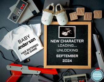 May include: A black and white ultrasound image is displayed on a letter board with the text "NEW CHARACTER LOADING... UNLOCKING SEPTEMBER 2024". A white onesie with the text "BABY Anderson HAS ENTERED THE GAME" is also in the image. The image is surrounded by various video game accessories, including a controller, a game cartridge, and a pair of baby shoes.