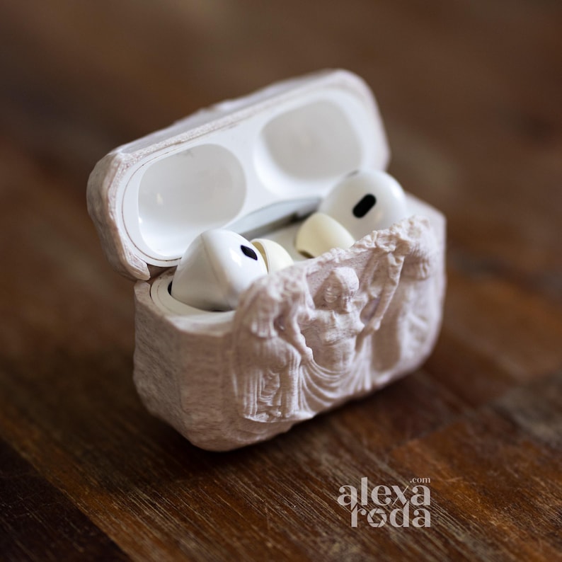 K&ouml;nnte beinhalten: Wei&szlig;e kabellose Ohrh&ouml;rer in einem hellbeigen Etui mit einem Reliefdesign. Das Etui ist ge&ouml;ffnet und zeigt die Ohrh&ouml;rer und das Innere. Das Etui liegt auf einer Holzoberfl&auml;che.