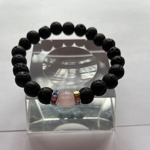 Può includere: Braccialetto con perline di roccia lavica nera, una perla di cristallo rosa e dettagli argentati.