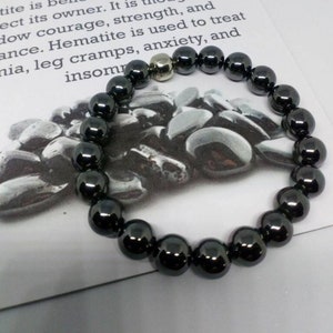 May include: A black hematite bracelet with a silver bead. The bracelet is on a white card with text about the benefits of hematite.