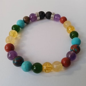 May include: A rainbow chakra bracelet with seven different coloured beads, including red, orange, yellow, green, blue, indigo, and violet. The bracelet also features two silver spacers with a Greek key design.