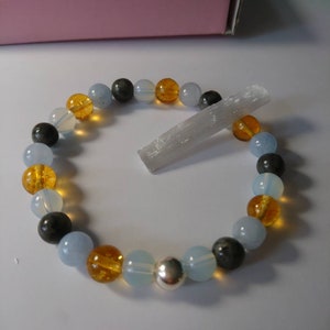 May include: A bracelet made with blue, gray, and amber beads, with a silver charm. A clear crystal is also included.