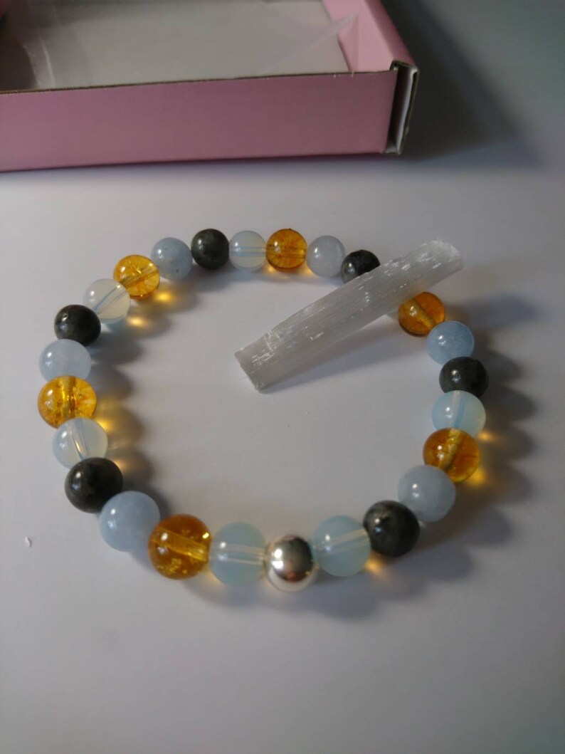 May include: A bracelet made with blue, gray, and amber beads, with a silver charm. A clear crystal is also included.