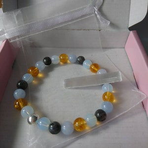 May include: A bracelet made of blue, orange, and gray beads in a clear organza bag. The bracelet is in a pink and white gift box.