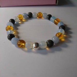 May include: A beaded bracelet with blue, yellow, and black beads. The bracelet has a silver charm in the center.