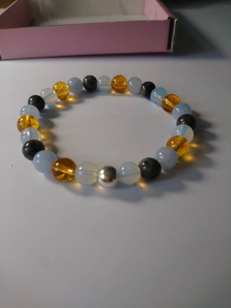 May include: A beaded bracelet with blue, yellow, and black beads. The bracelet has a silver charm in the center.