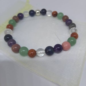May include: A multi-colored beaded bracelet with a silver charm. The bracelet features beads in shades of green, purple, brown, and white.