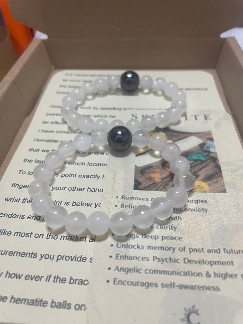 Pu&ograve; includere: Un braccialetto di perline bianche e nere con due sfere di ematite. Il braccialetto &egrave; in una scatola con un cartoncino che recita "Selenite" e elenca i benefici della pietra. I benefici includono: rimuove le energie negative, allevia l'ansia, porta una pace profonda, sblocca la memoria del passato e del futuro, migliora lo sviluppo psichico, comunicazione angelica e guida superiore, incoraggia la consapevolezza di s&eacute;.