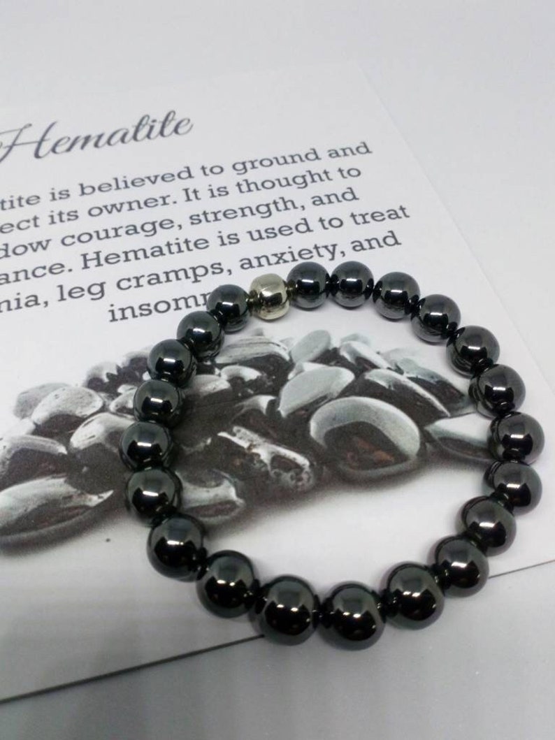 May include: A black hematite bracelet with a silver bead. The bracelet is on a white card with text about the benefits of hematite.