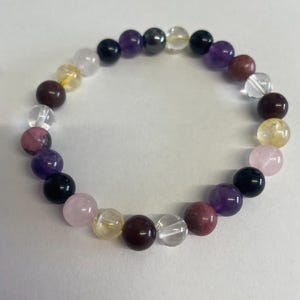 May include: A bracelet made of various coloured gemstone beads, including purple, pink, clear, yellow, and brown.