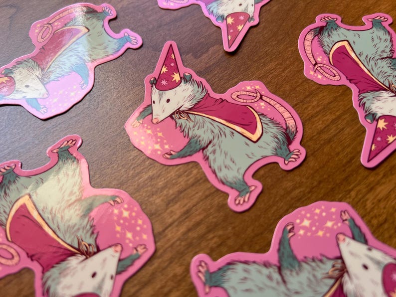 May include: A set of six pink and white stickers featuring cartoon possums wearing wizard hats and capes. The possums are holding wands and casting spells. The stickers are ideal for adding a touch of whimsy to your laptop, water bottle, or planner.